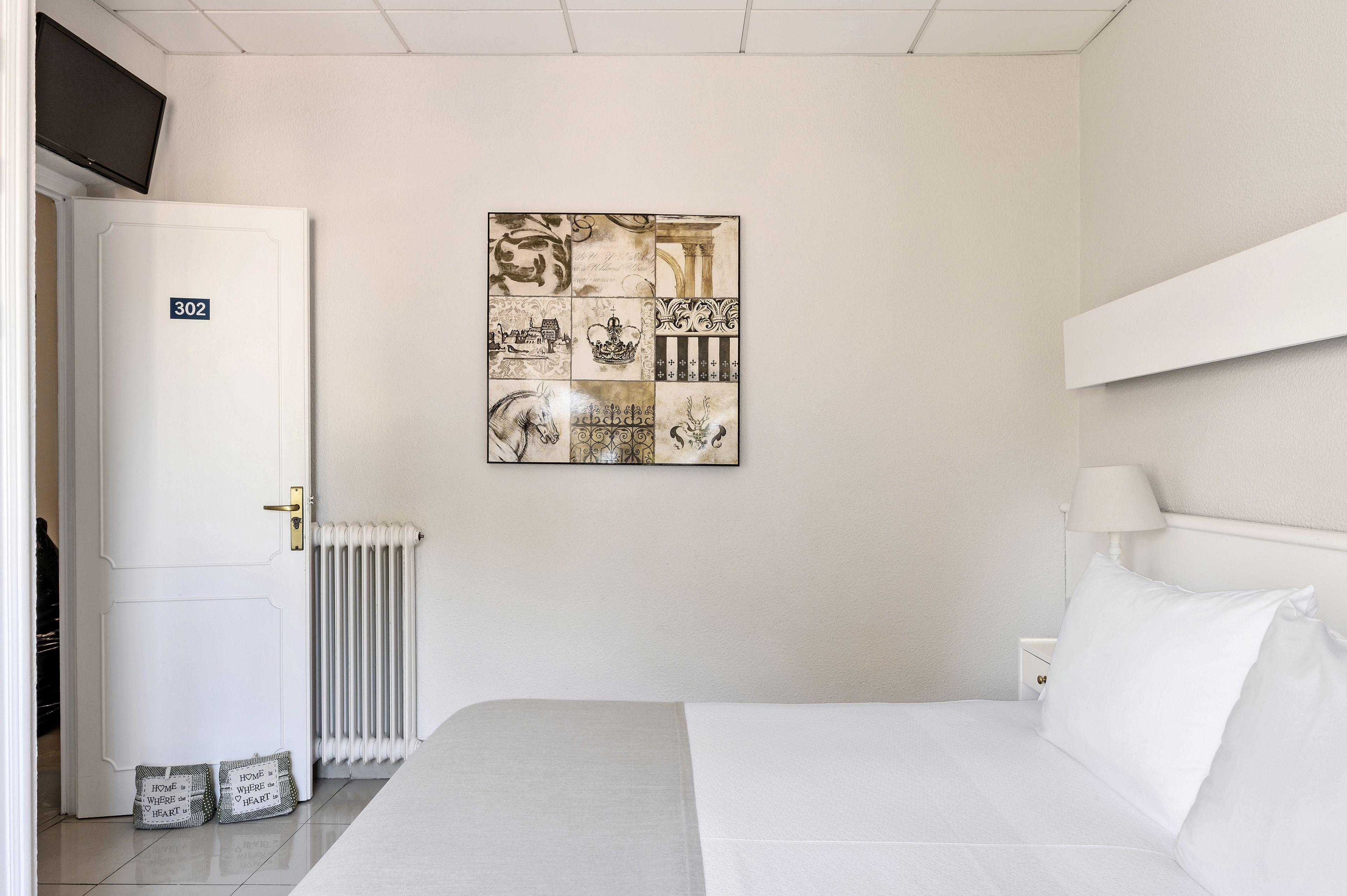 A hotel room with a bed, a wall-mounted artwork, a door labeled 302, a radiator, and a nightstand with a lamp.