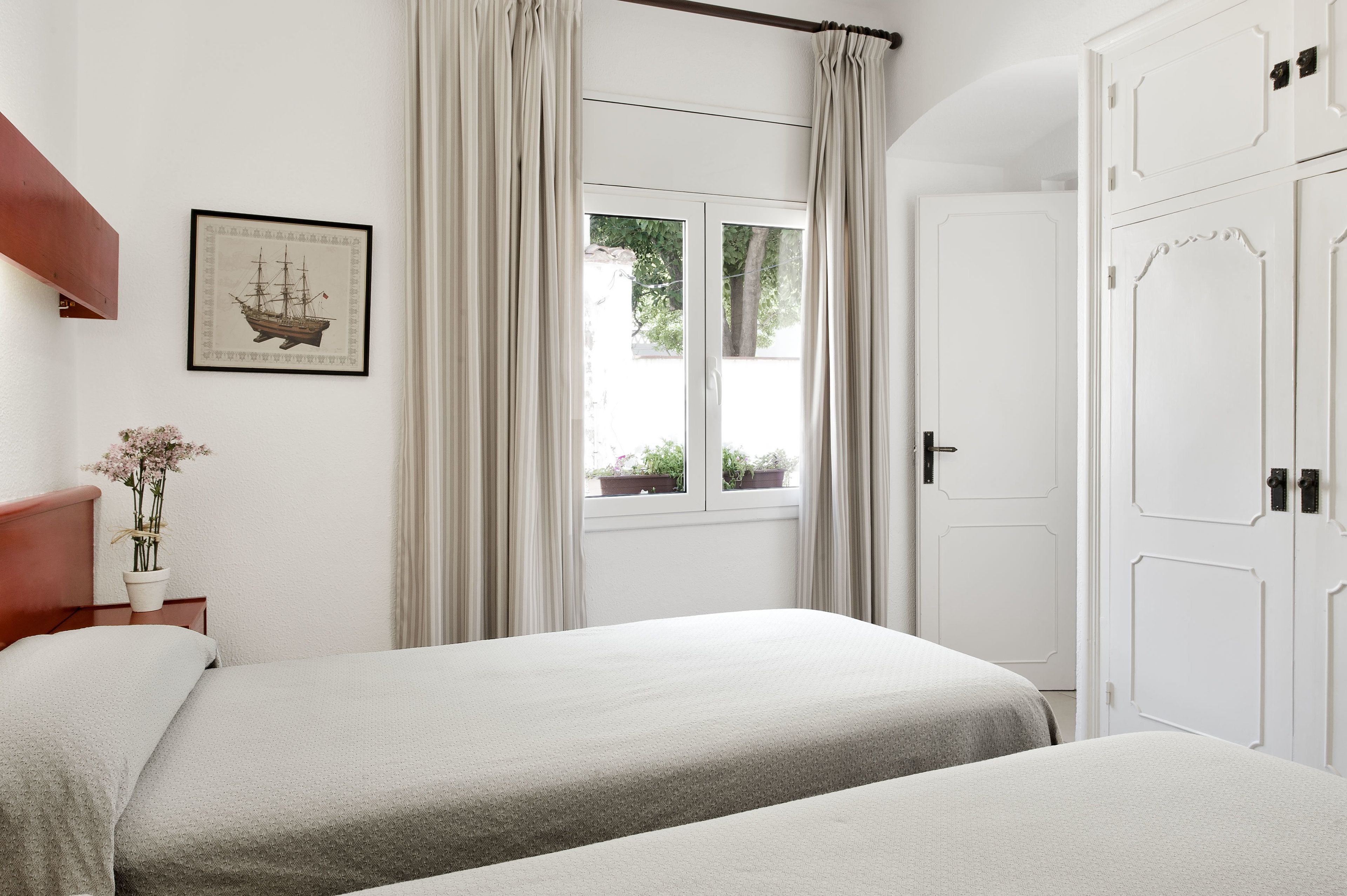 A bedroom with two beds, a window with curtains, a door, and a framed picture on the wall.