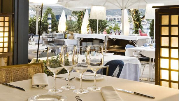 A dining table set with wine glasses, plates, and cutlery, overlooking a scenic view with umbrellas and outdoor seating. - Hotel La Goleta (Llanca)