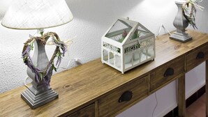 A wooden console table with two lamps, a decorative wreath, and a white storage box against a white wall. - Hotel La Goleta (Llanca)