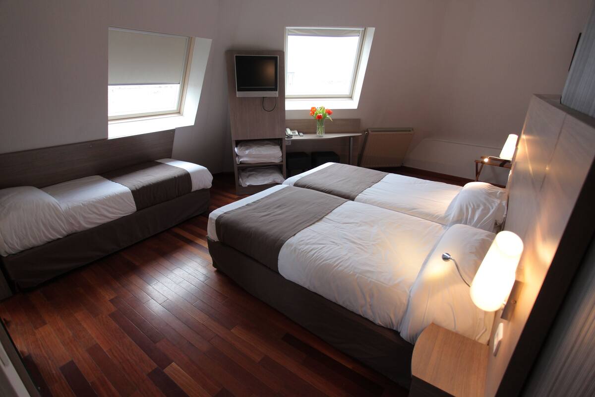 Ein Hotelzimmer mit zwei Betten, einem Schreibtisch, einem Fernseher und einem Fenster mit Aussicht.