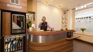 A hotel reception desk with a coffee shop vending machine, a clock, and a window with a view of a ship. - Grand Hôtel du Loiret (Paris)