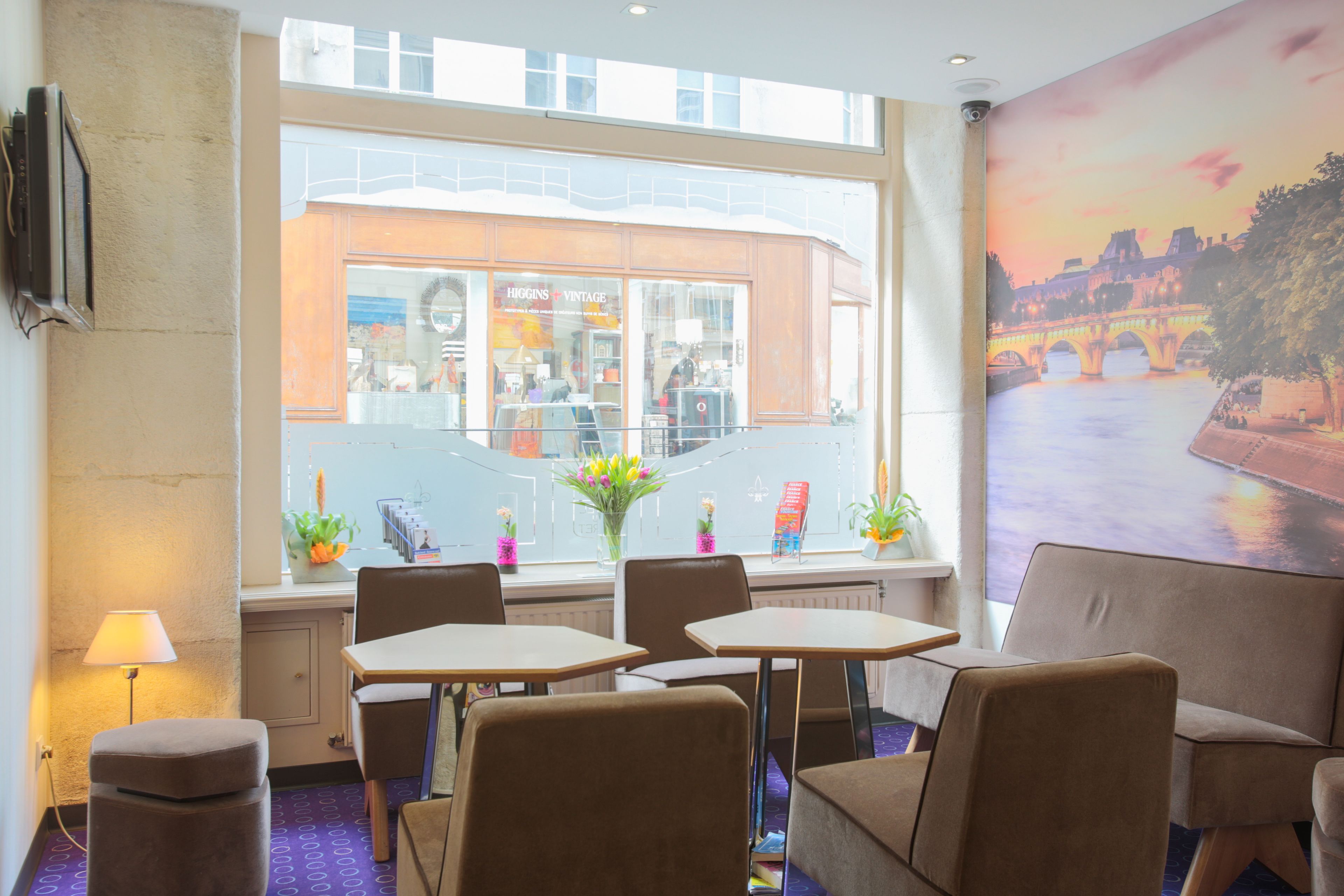 A restaurant with tables and chairs, a window with a view of a building, and a mural of a bridge.