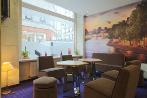 A hotel room with a large window overlooking a street, a mural of a river scene, and a seating area with a table and chairs. - Grand Hôtel du Loiret (Paris)