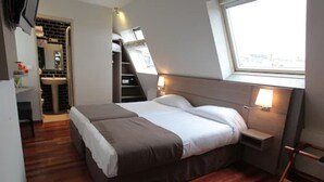 A bedroom with a large bed, a window, a built-in desk, and a bathroom with a sink and mirror. - Grand Hôtel du Loiret (Paris)