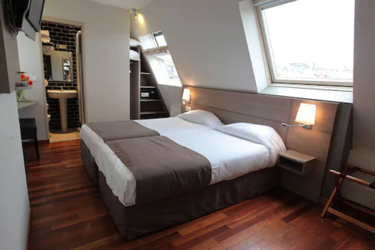 Ein Schlafzimmer mit einem großen Bett, einem Fenster, einem integrierten Schreibtisch und einem Badezimmer mit Waschbecken und Spiegel.