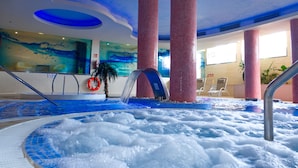 Un área interior con jacuzzi, suelo de mosaico azul, pilares rojos y una cascada.