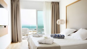 Habitación de hotel con cama, televisión, balcón y vistas al mar, además de una lámpara.