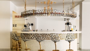 Zona de bar con una lámpara original, taburetes y una encimera blanca.