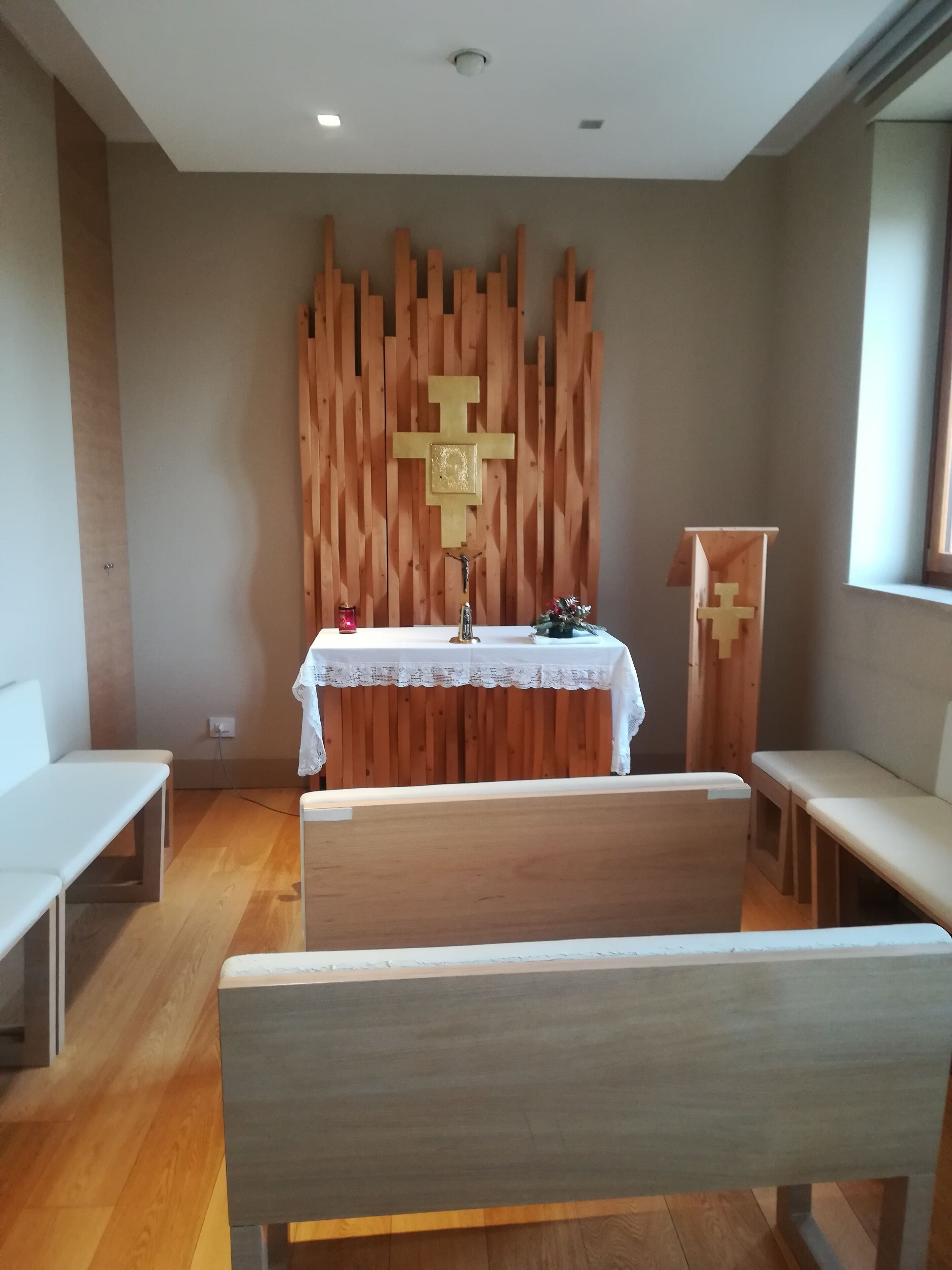 A church interior with wooden pews, a white altar table, and a wooden cross on the wall.