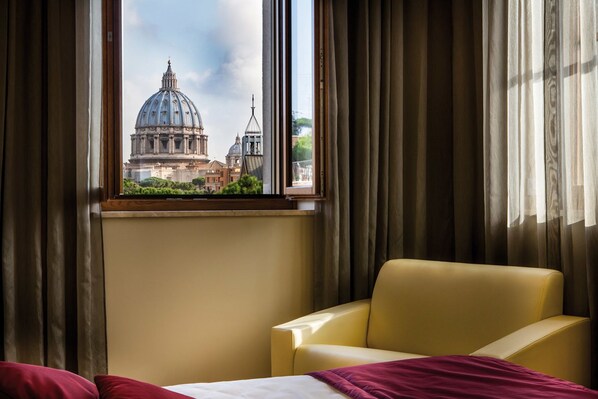 Une chambre d’hôtel avec une grande fenêtre, un fauteuil jaune et un lit avec des oreillers rouges.