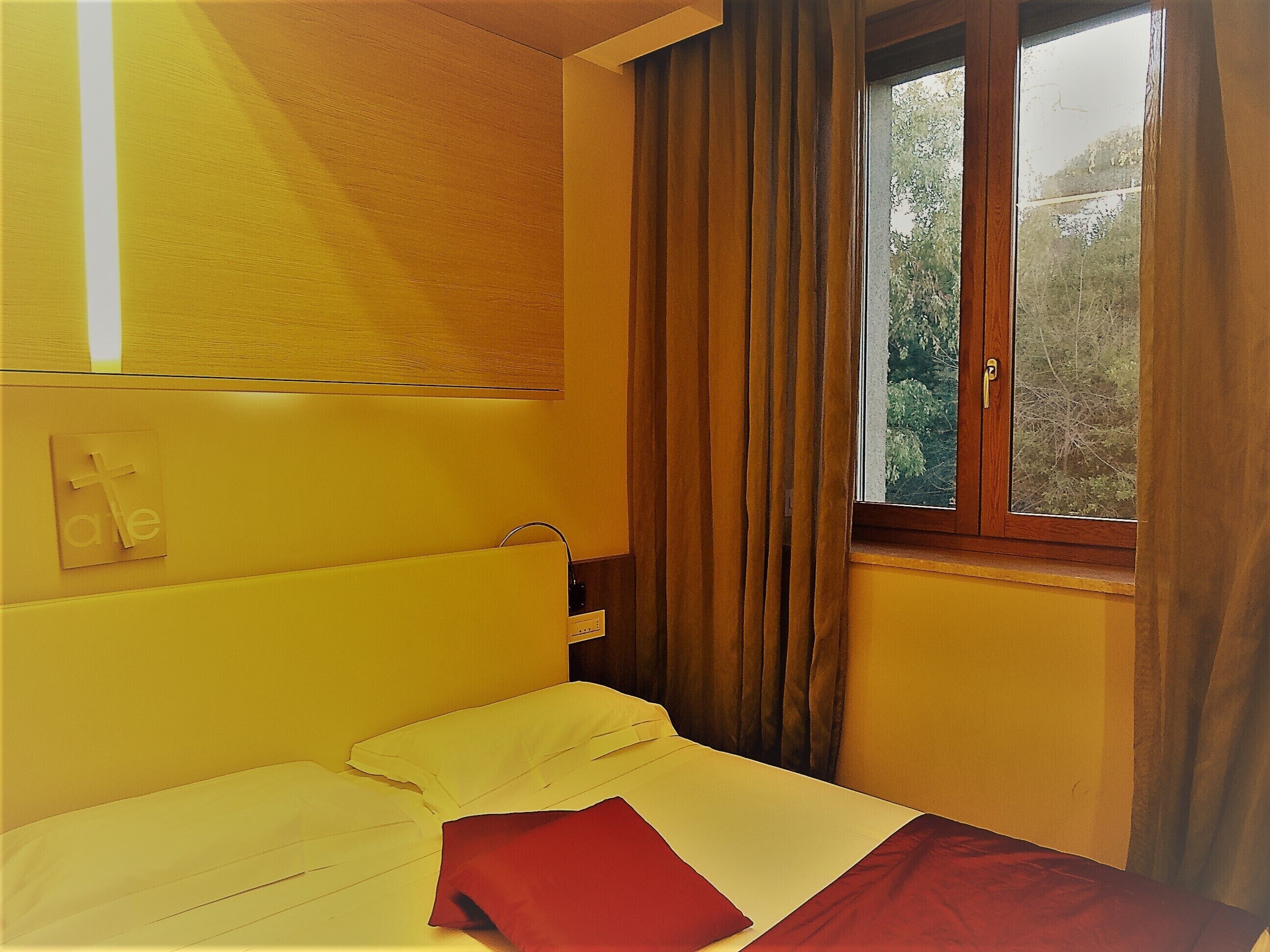 A room with a bed, a window with curtains, and a wall-mounted light switch.