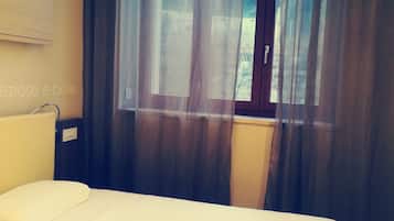 Una camera d'albergo con un letto, una finestra con tende e un lampadario a parete.