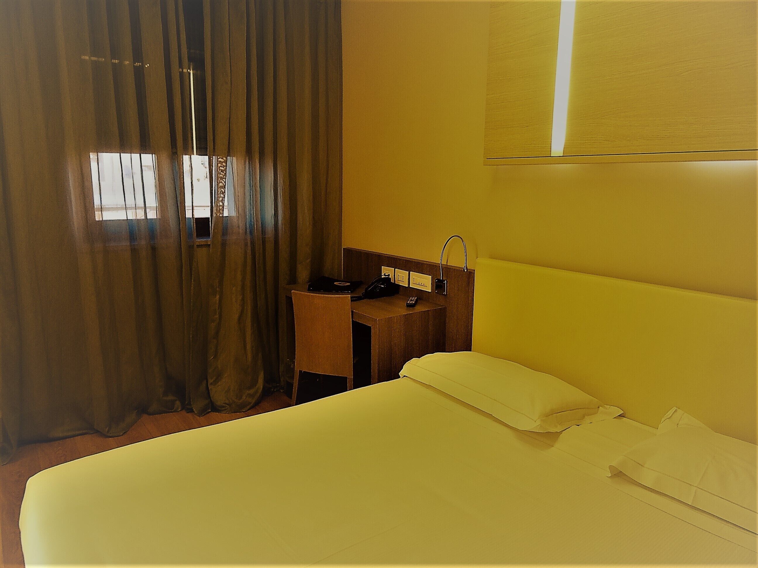Una camera d'albergo con un letto, una scrivania con il telefono e una finestra con tende.