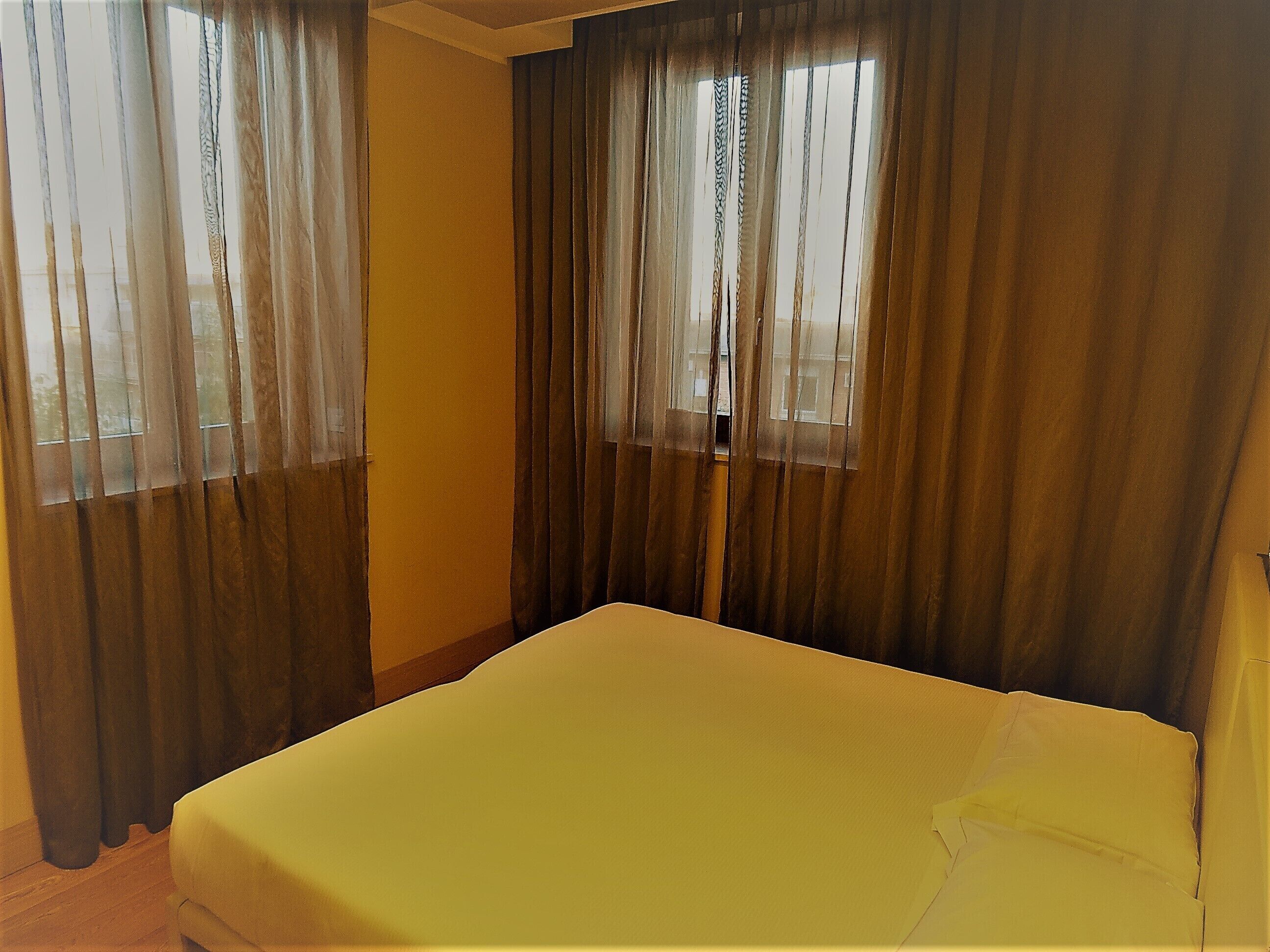 Una stanza con un letto, due finestre con tende e una parete spoglia.