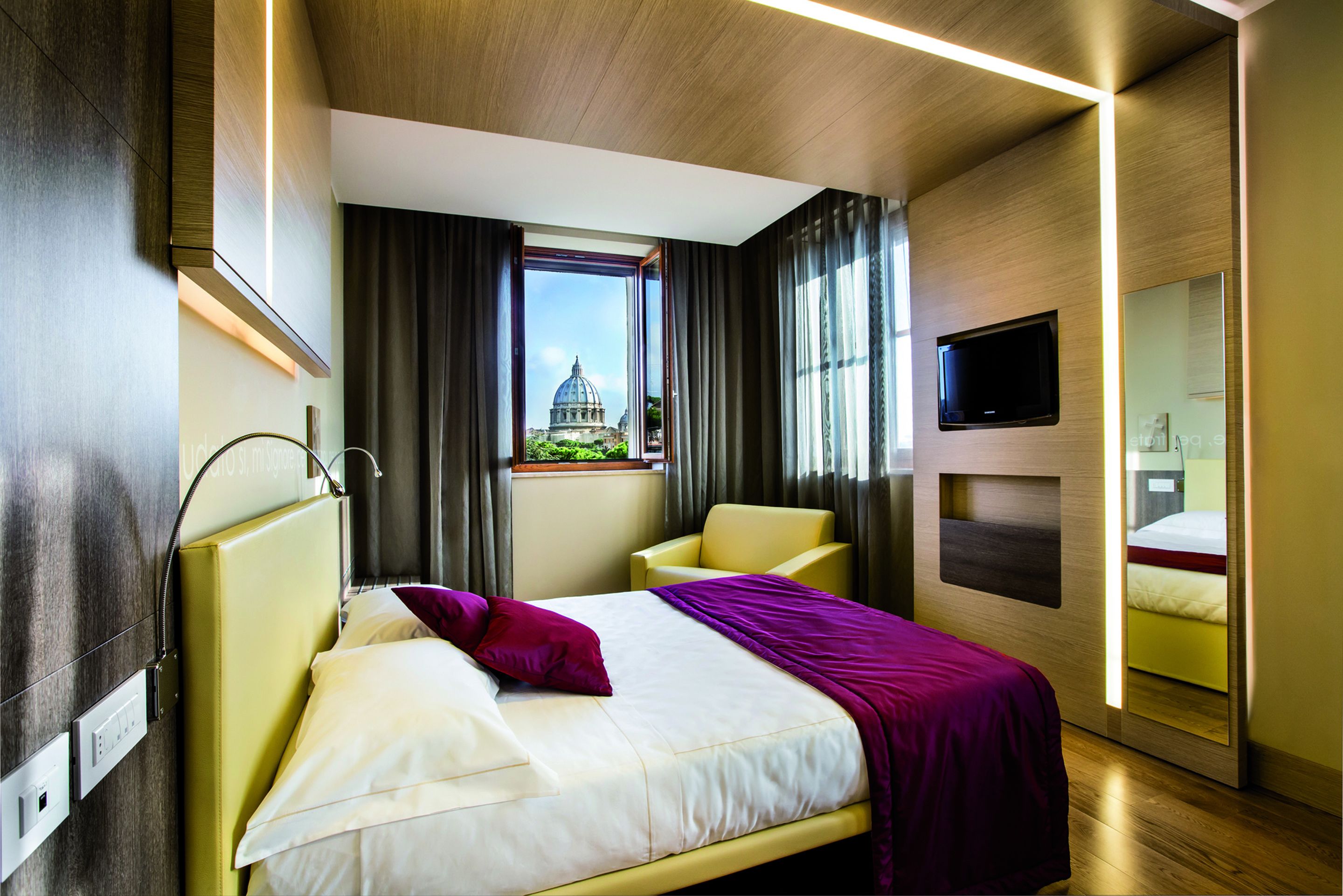 A modern hotel room with a bed, a chair, a TV, and a window with a view of a dome structure.