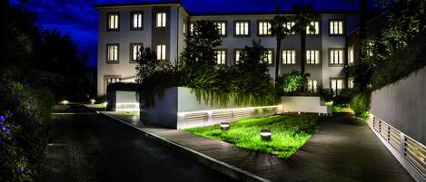 A modern building with multiple windows, a paved pathway, and a landscaped area with grass and plants.
