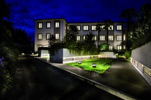 Moderni rakennus, jossa on useita ikkunoita, päällystetty kävelyreitti ja maisemoitu alue, jossa on nurmikkoa ja kasveja.