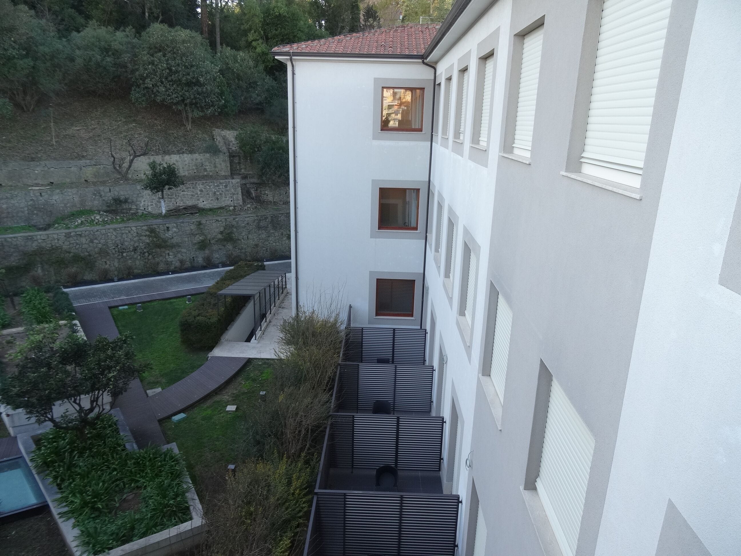 Un edificio de varios pisos con un patio interior, un muro de piedra de contención y un sendero pavimentado.