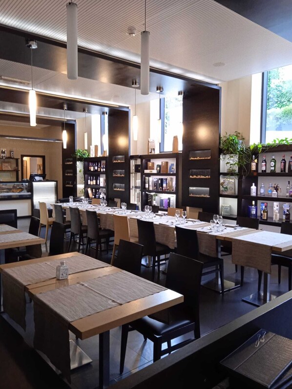 A modern restaurant with long communal tables, black chairs, and pendant lighting. - Hotel Il Cantico St. Peter (Rome)