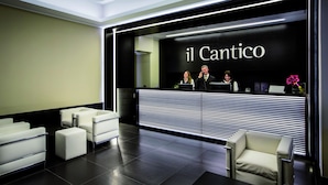 A reception area with a black and white striped counter, white seating, and a sign reading "il Cantico".