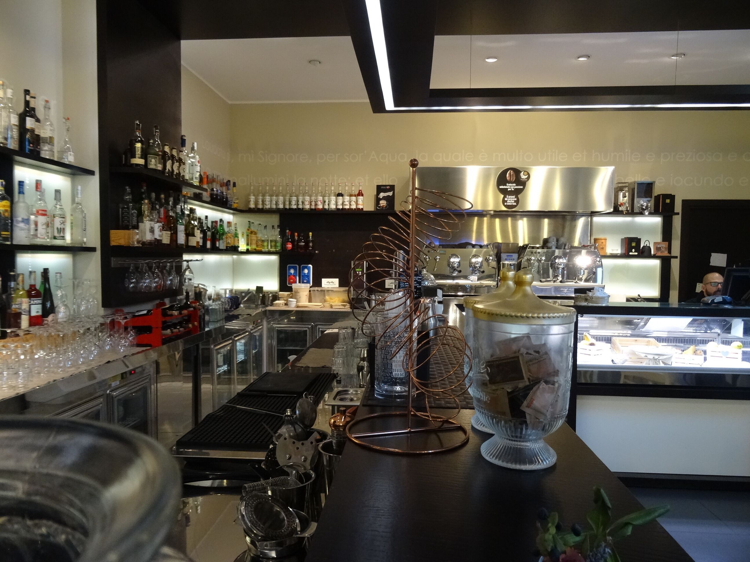 A bar area with shelves of liquor bottles, a coffee machine, and a display case with food items.