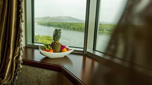 A bowl of fruit on a windowsill with a view of a lake and mountains. - Hayat Hospitality Oskemen (Oskemen)