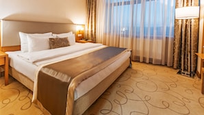 A hotel room with a large bed, a nightstand, a lamp, and a view of the outdoors through sheer curtains. - Hayat Hospitality Oskemen (Oskemen)