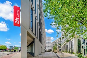 Un hôtel moderne, reconnaissable à son grand panneau rouge, situé dans un quartier urbain propre et bénéficiant d’un ciel dégagé.