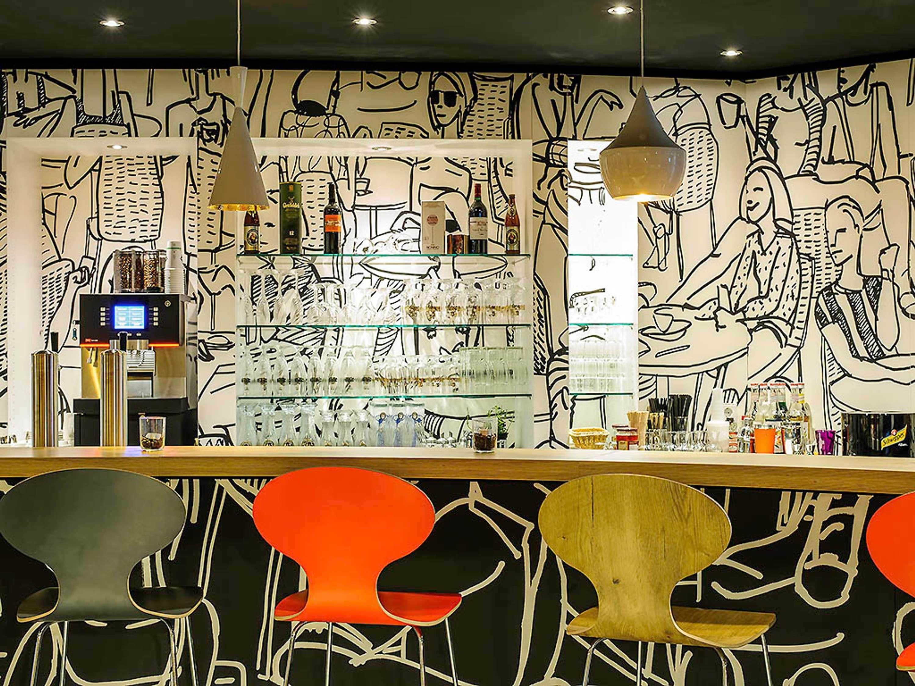 Un espace bar comprenant un comptoir, des tabourets de bar et un mur décoré de dessins au trait en noir et blanc.