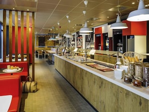 Zona de bufé con mostrador de madera, diferentes opciones de comida y disposición de mesas y sillas.
