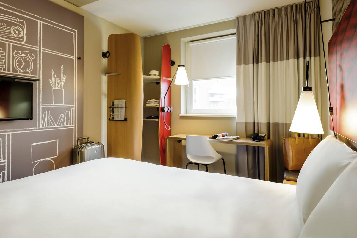 Hotelkamer met een bed, bureau, stoel, televisie, kast en raam met gordijnen.