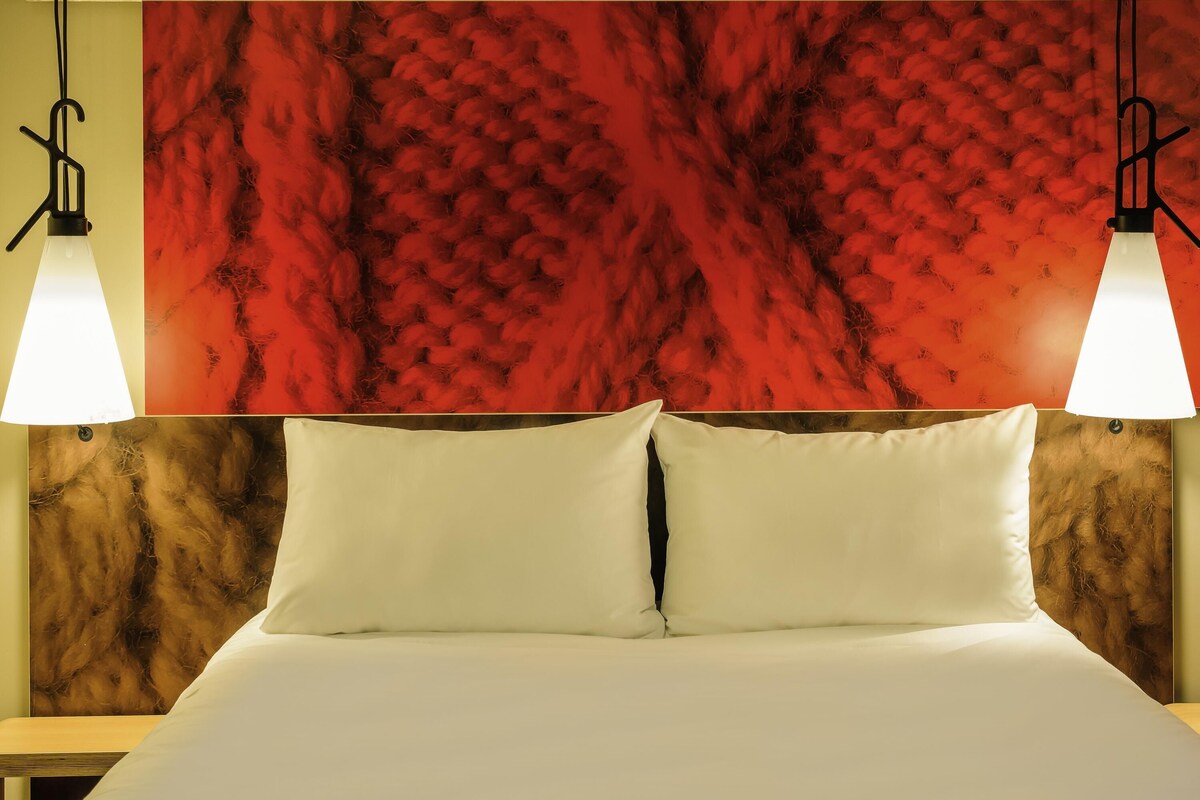 Un lit avec une literie blanche, deux lampes de chevet et un mur rouge à texture en arrière-plan.