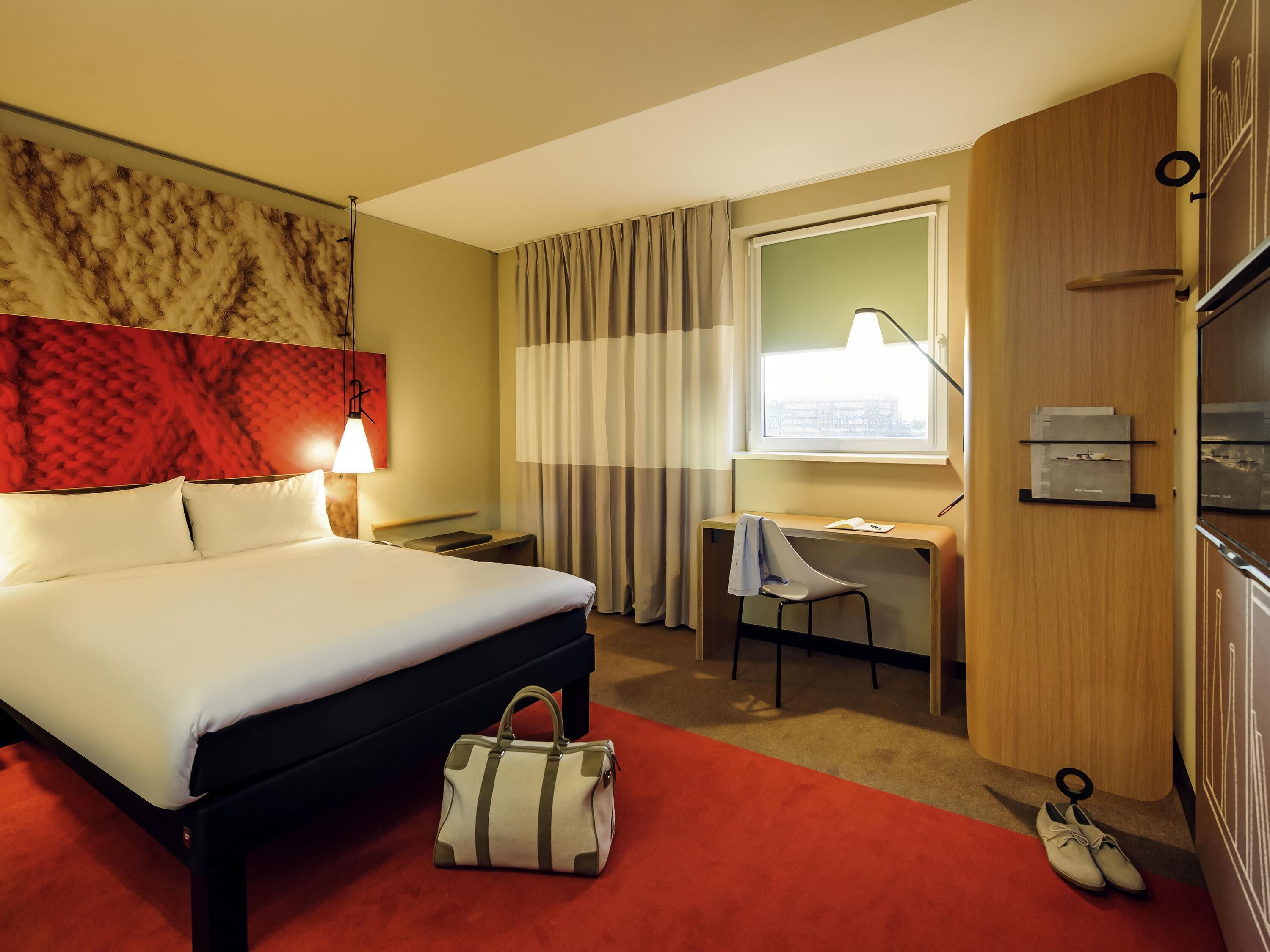 Habitación de hotel con cama, escritorio, silla y vista a la ciudad por la ventana.