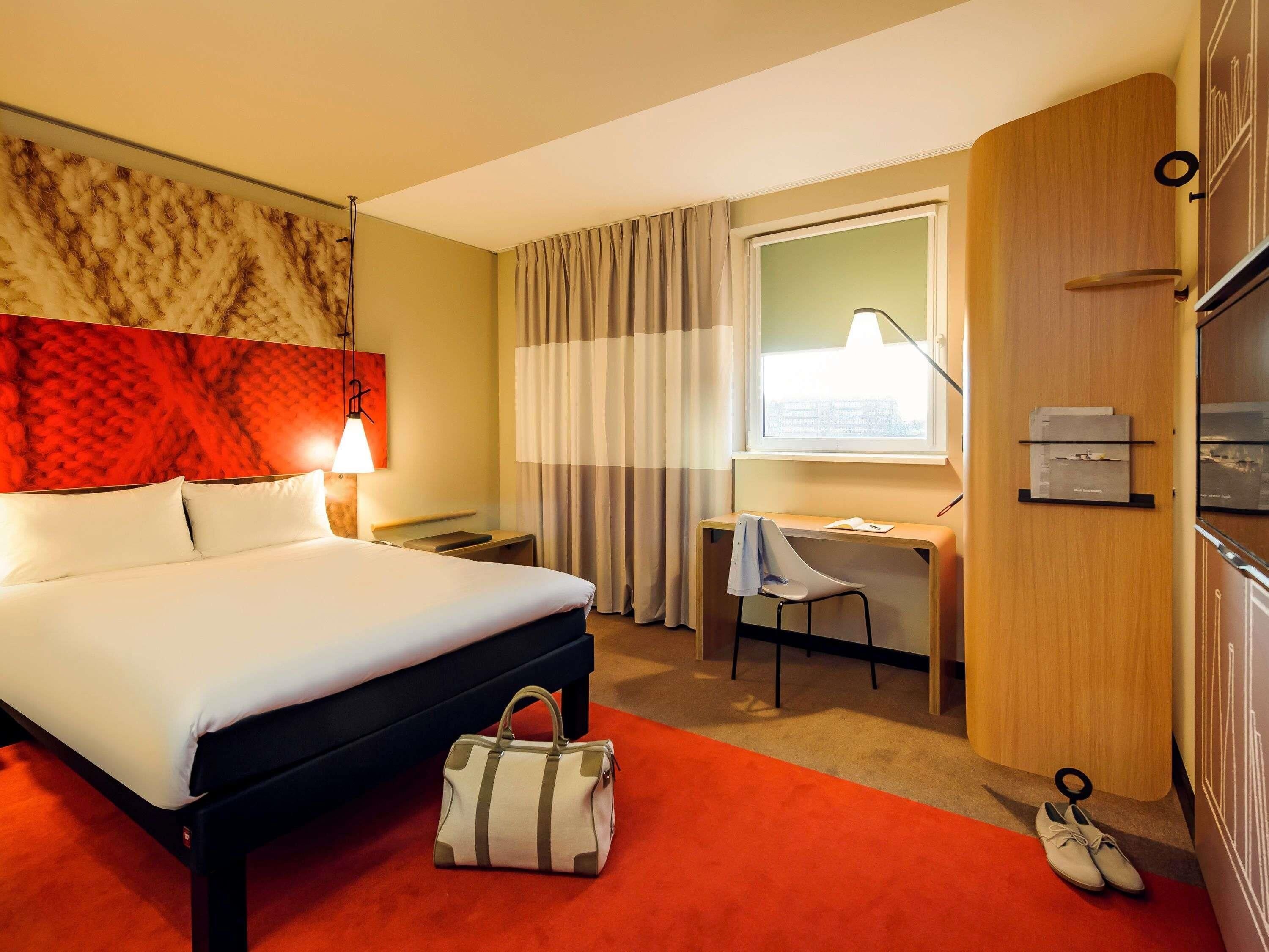 A hotel room with a bed, desk, chair, and a suitcase on the floor.