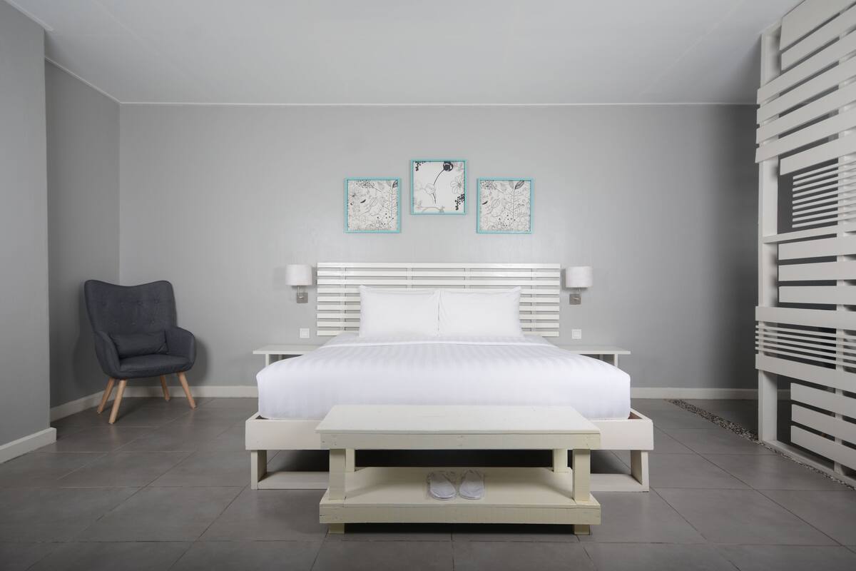 A modern bedroom with a white bed, a grey armchair, and a small table with shoes on it.