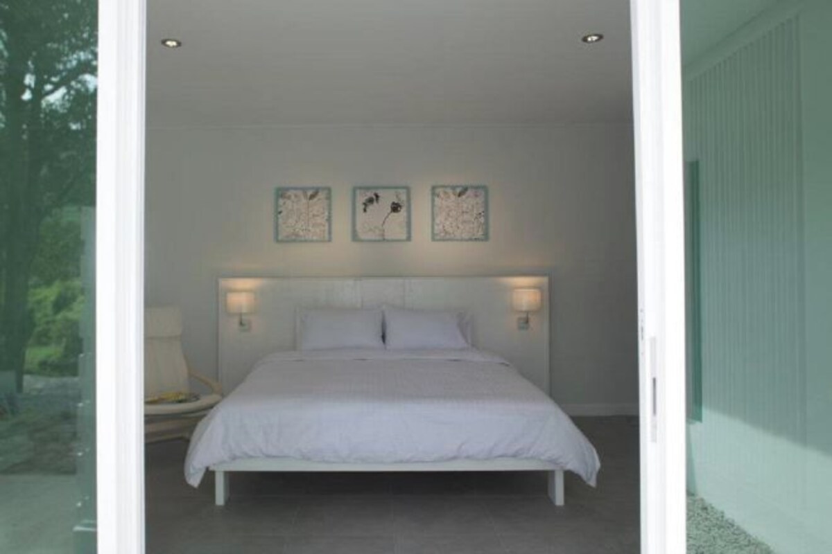 A bedroom with a bed, two wall-mounted lamps, and three framed pictures on the wall.