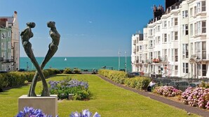 Un paseo marítimo con una escultura, una hilera de edificios blancos y una vista despejada del mar.