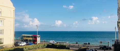 A coastal view with a road, parked cars, a bus, and a building.