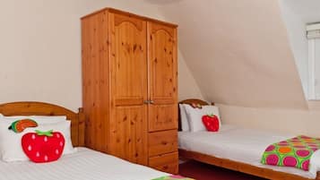 A bedroom with two single beds, each with a colorful bedspread and a strawberry-themed pillow. A wooden wardrobe is present, and the room has a sloped ceiling.