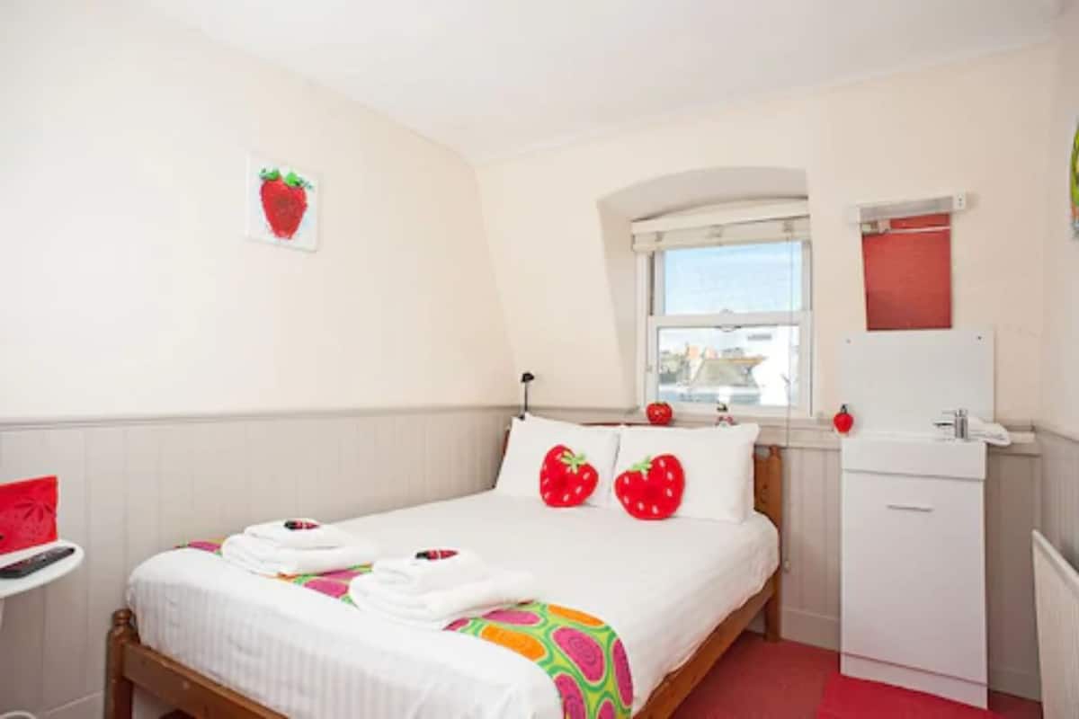 Un dormitorio ordenado con cama, un escritorio pequeño y una ventana.