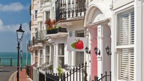 Una hilera de edificios blancos con balcones, un sendero de ladrillo rojo y un cielo azul despejado.