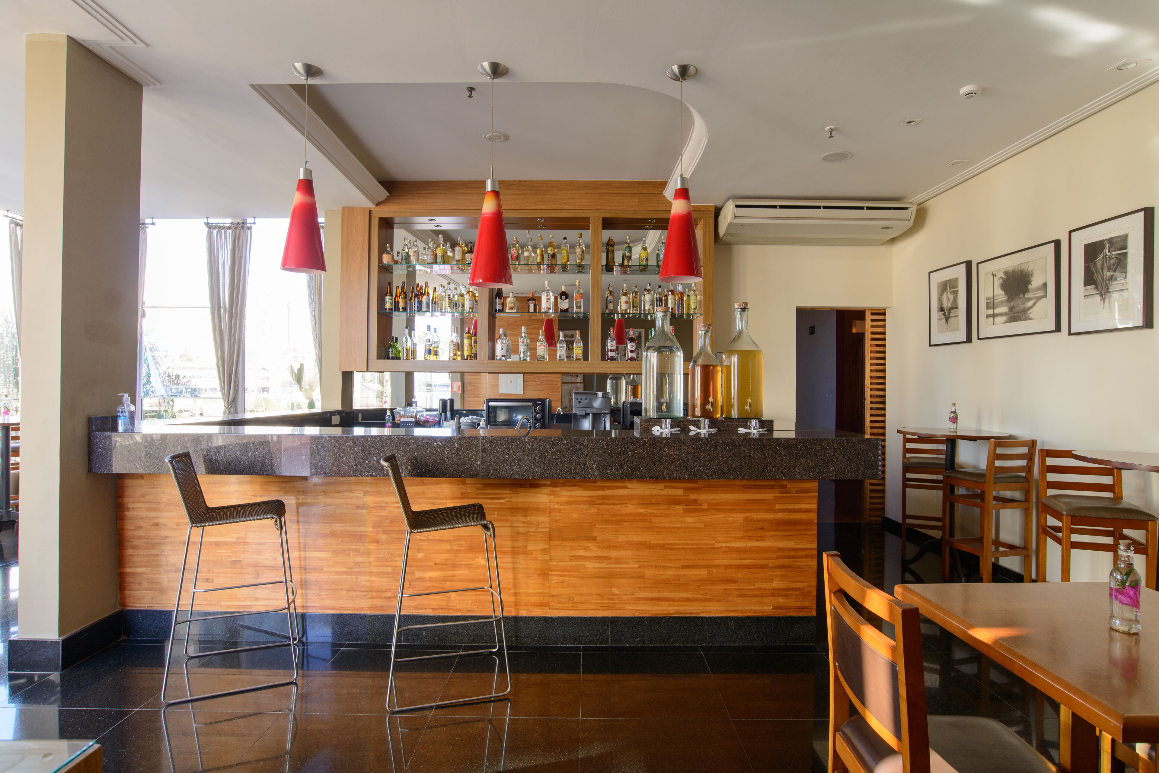 Zona de bar con mostrador de madera, dos taburetes y lámparas colgantes rojas.