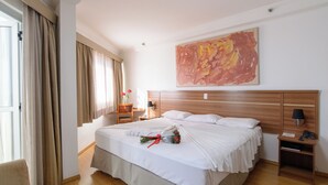 A hotel room with a large bed, a wooden headboard, a nightstand with a lamp, and a painting on the wall. - Faro Hotel São José dos Campos (São José dos Campos)