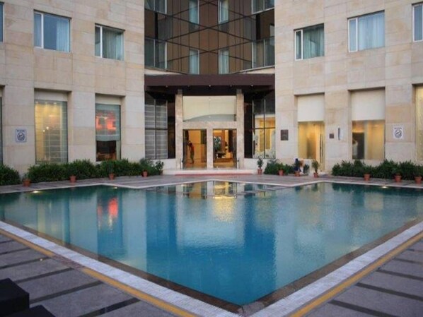 Un hotel con piscina central, acceso cubierto y diseño arquitectónico moderno.
