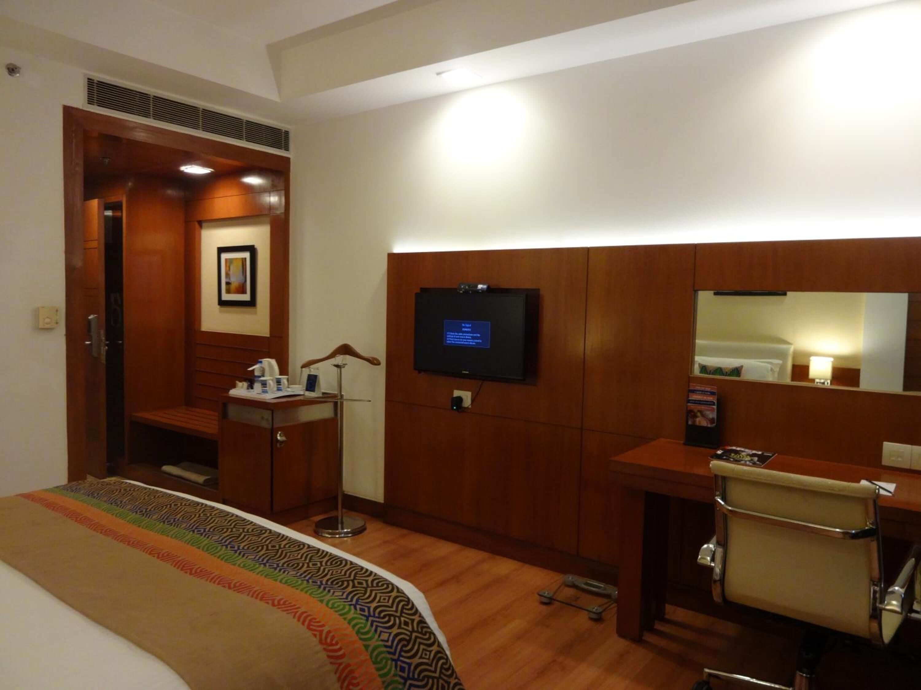 Una habitación de hotel con una cama, un escritorio, una silla, un televisor y un espejo.