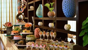 Een buffet met diverse desserts en drankjes, een decoratieve muur met vazen, en een plant.