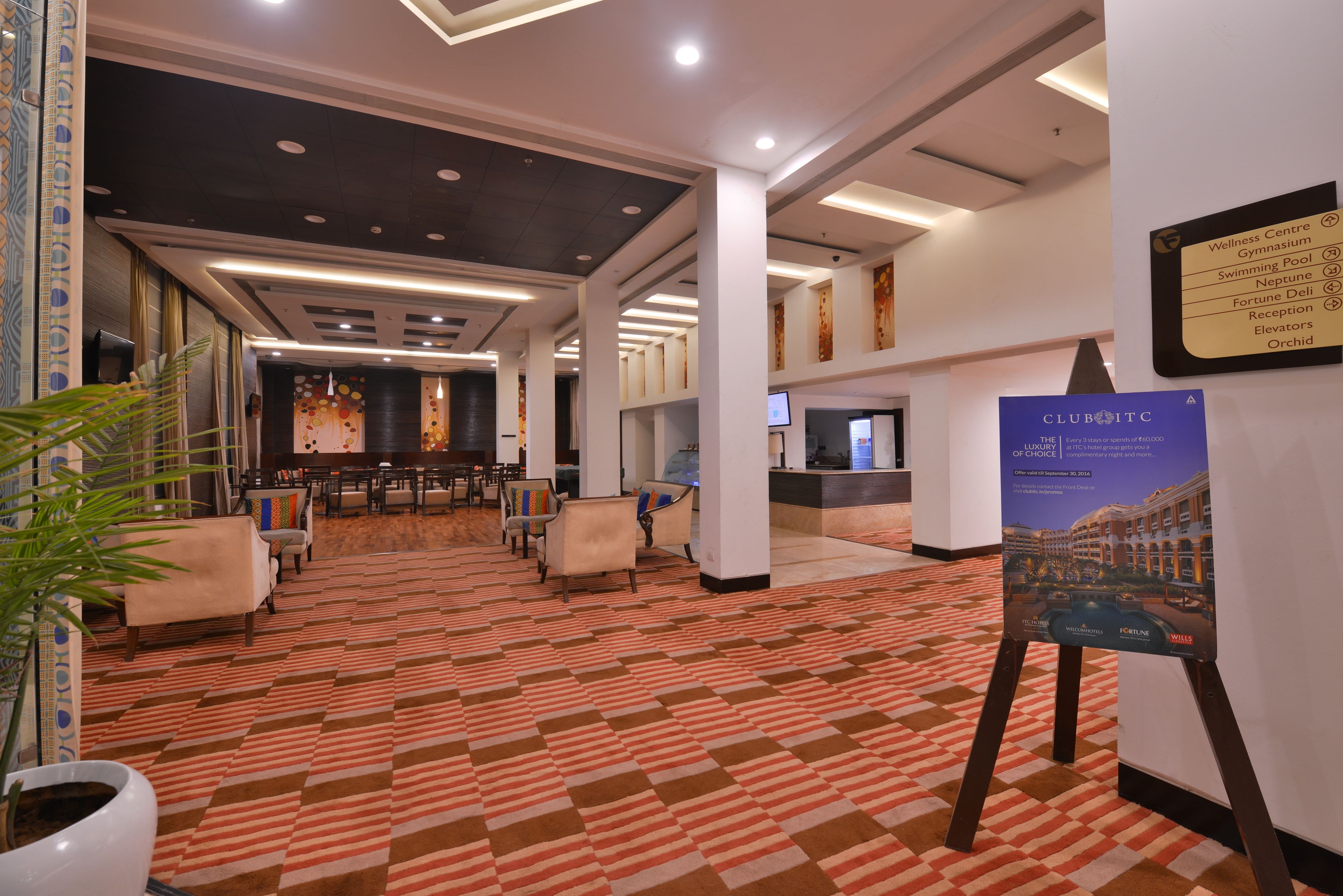 Vestíbulo de hotel con alfombra estampada, zona de estar, mostrador de recepción y un cartel.