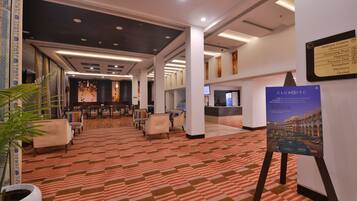 Vestíbulo de hotel con alfombra estampada, zona de estar, mostrador de recepción y un cartel.