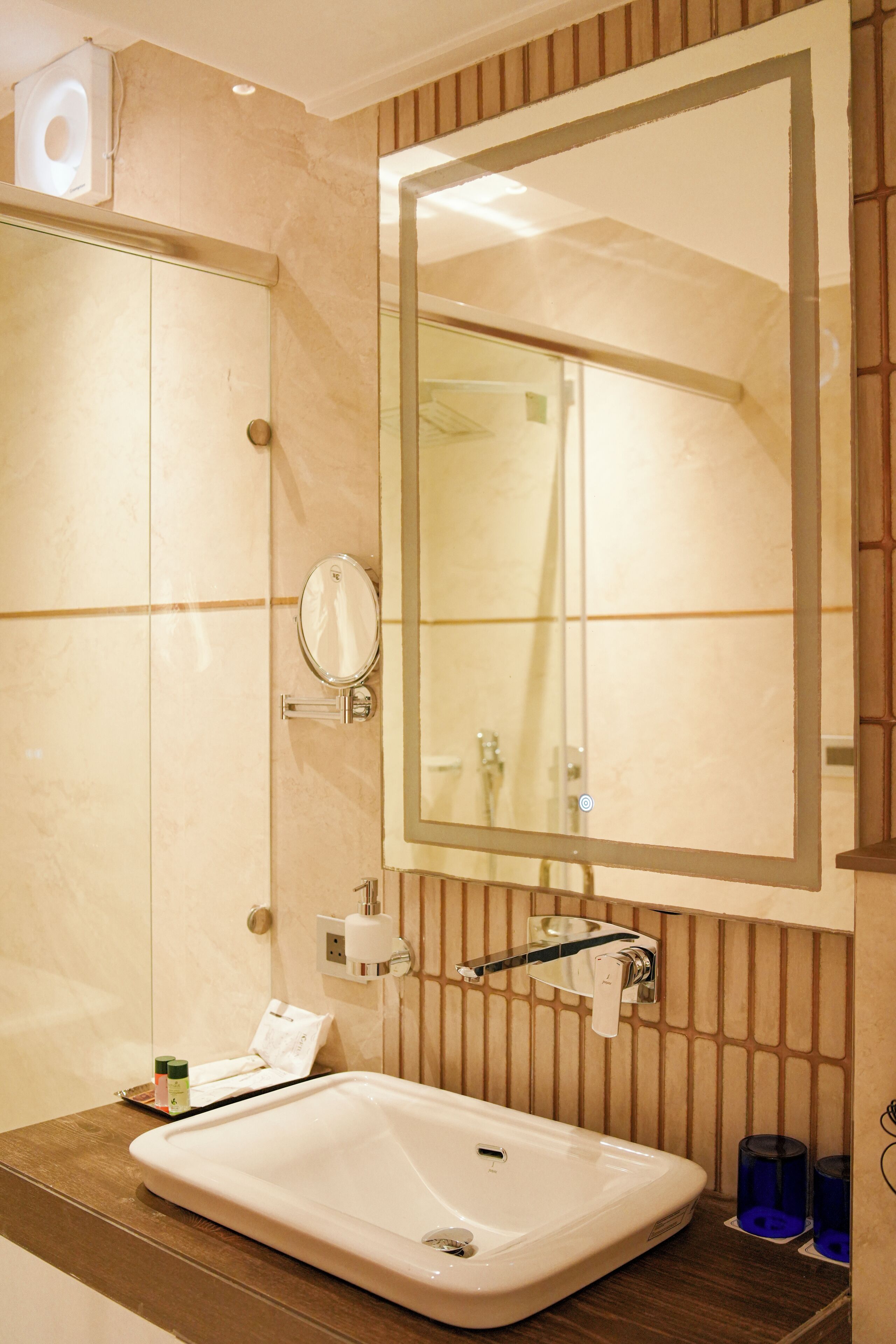 A bathroom with a large mirror, a sink, and a towel dispenser.
